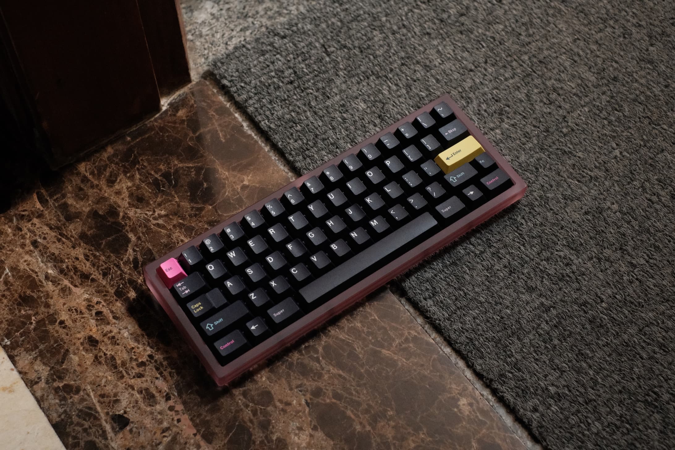 Pink polycarbonate mechanical keyboard with dark purple and yellow accent colored keycaps on marble floor
