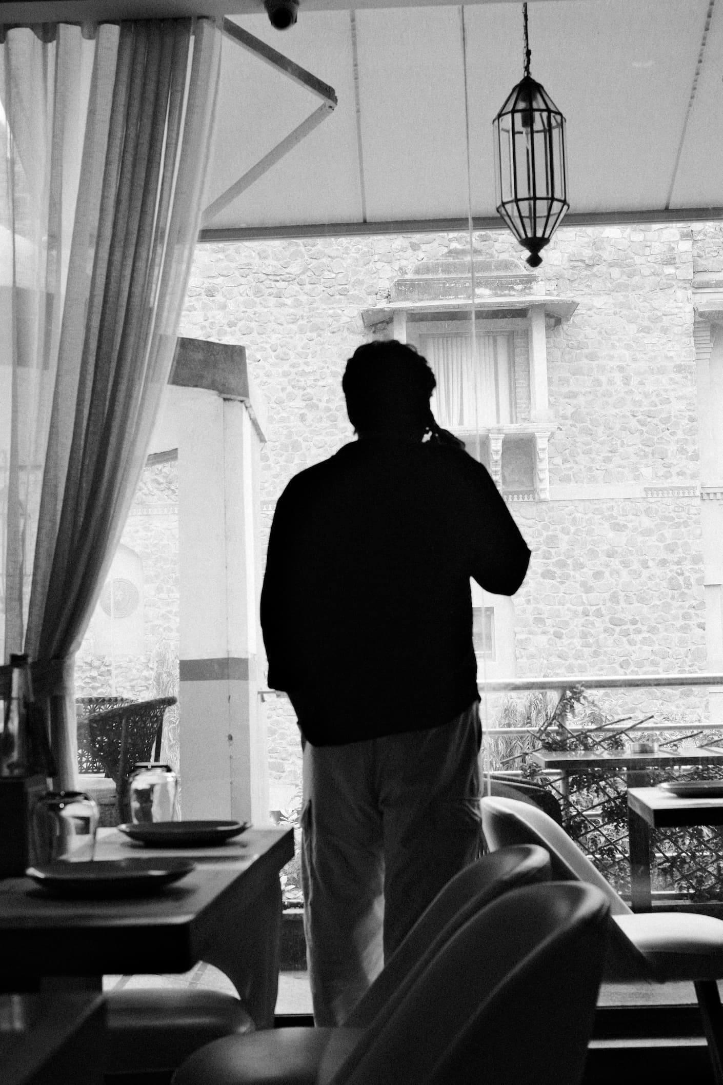Person silhouetted at window overlooking stone building in black and white photograph