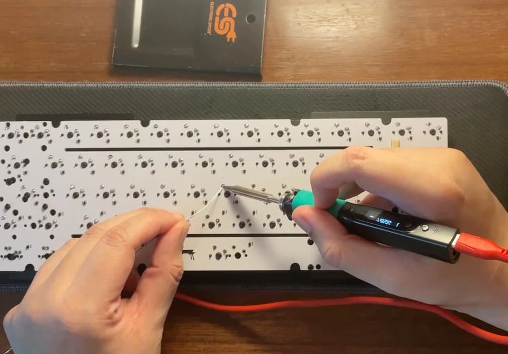 Soldering iron and solder over a PCB for a keyboard.