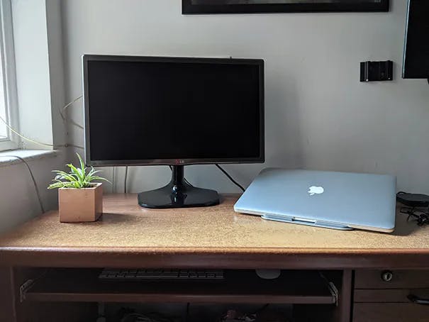 A desk with a old-school LCD monitor and a 2015 MacBook Pro on a stand