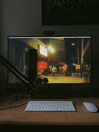A desk with a large LED monitor, Apple Magic Mouse and Keyboard and a microphone on a Mic stand clipped to the table